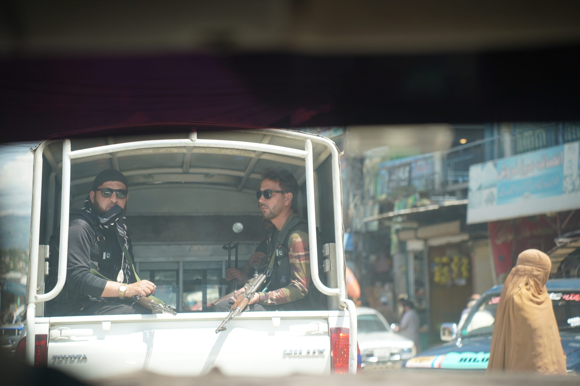 Armed officers riding in the back of a pickup through a busy street.