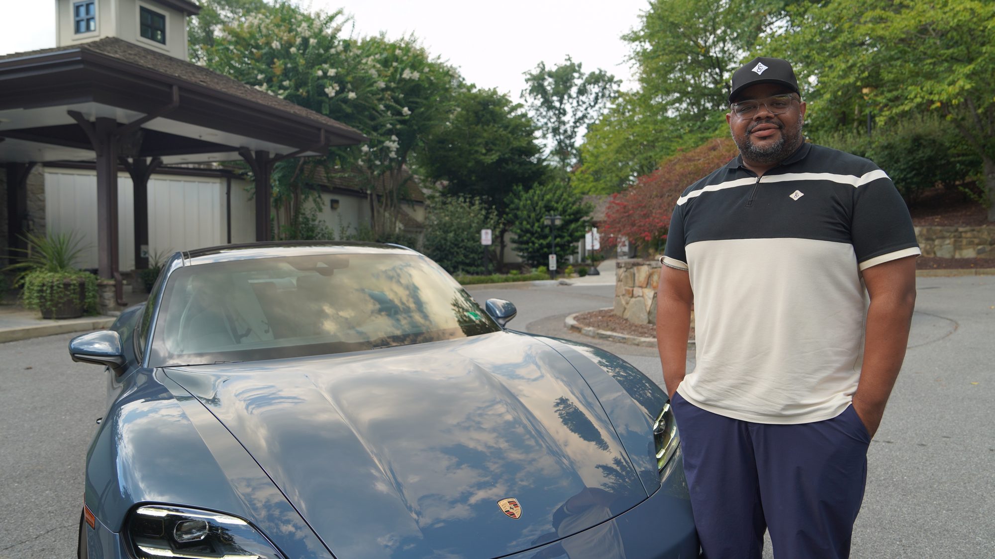 A resident standing beside a Porsche in a wooded suburban driveway.