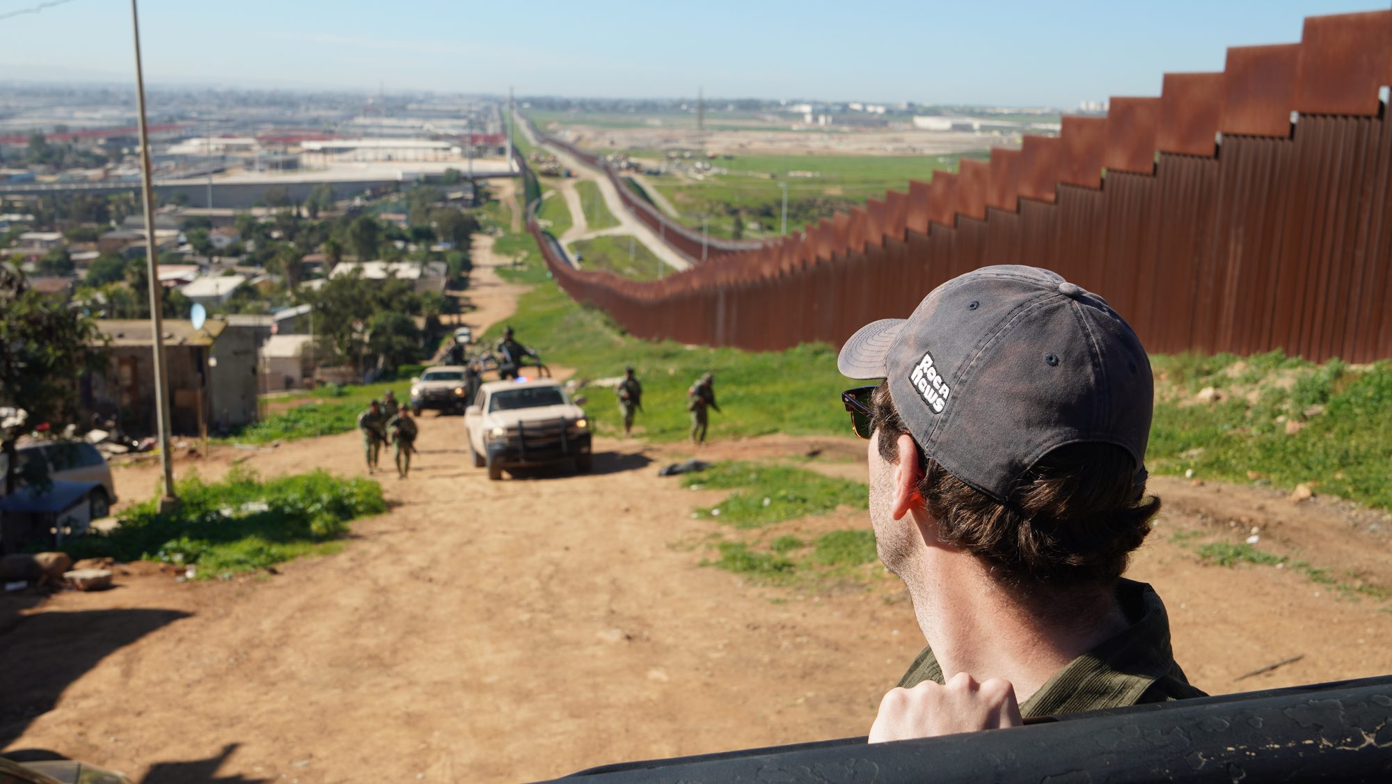 A Roca correspondent looking out over the border wall as Mexican forces move up a dirt road.